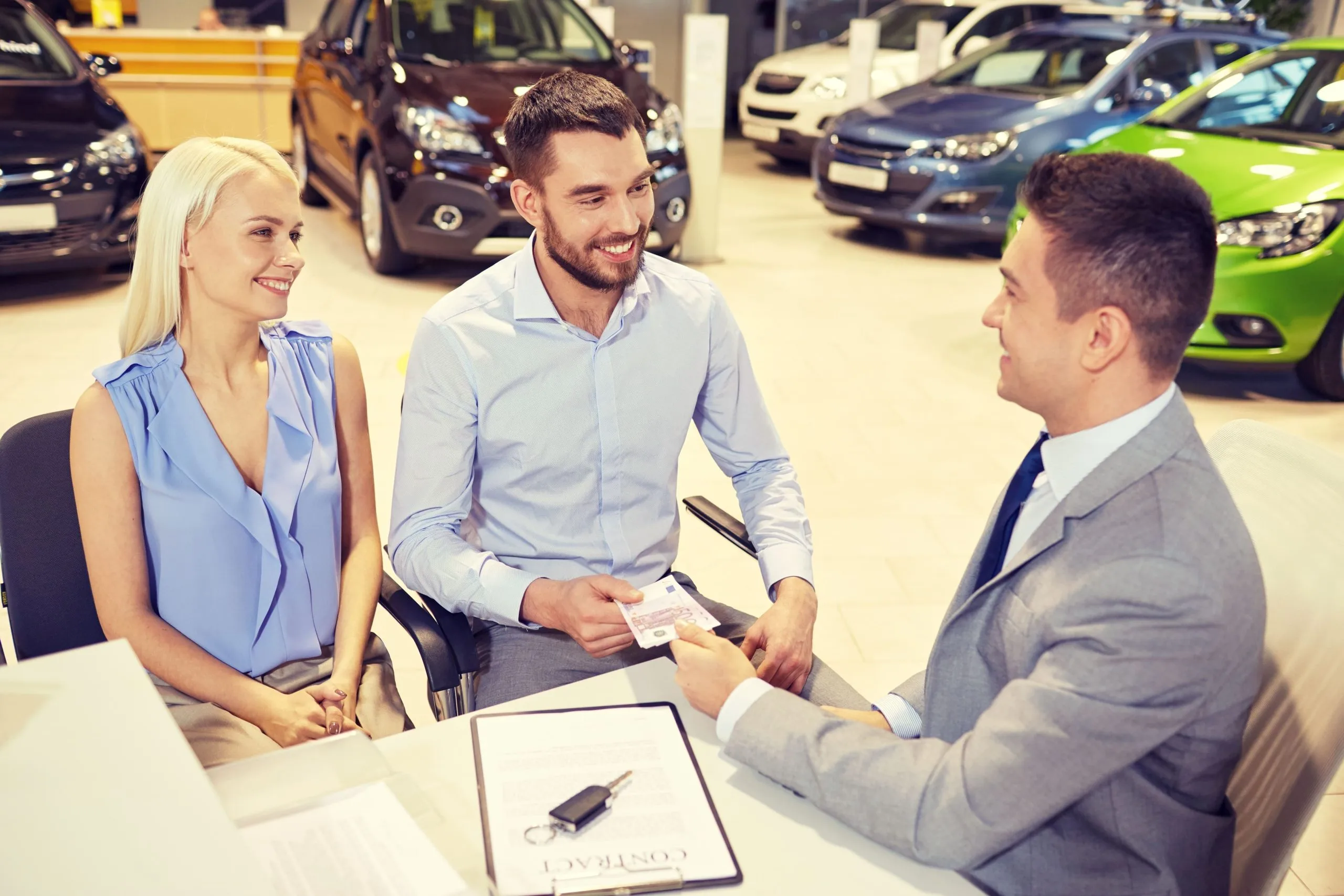 auto-business-sale-people-concept-happy-couple-with-dealer-buying-car-auto-show-salon-1-scaled