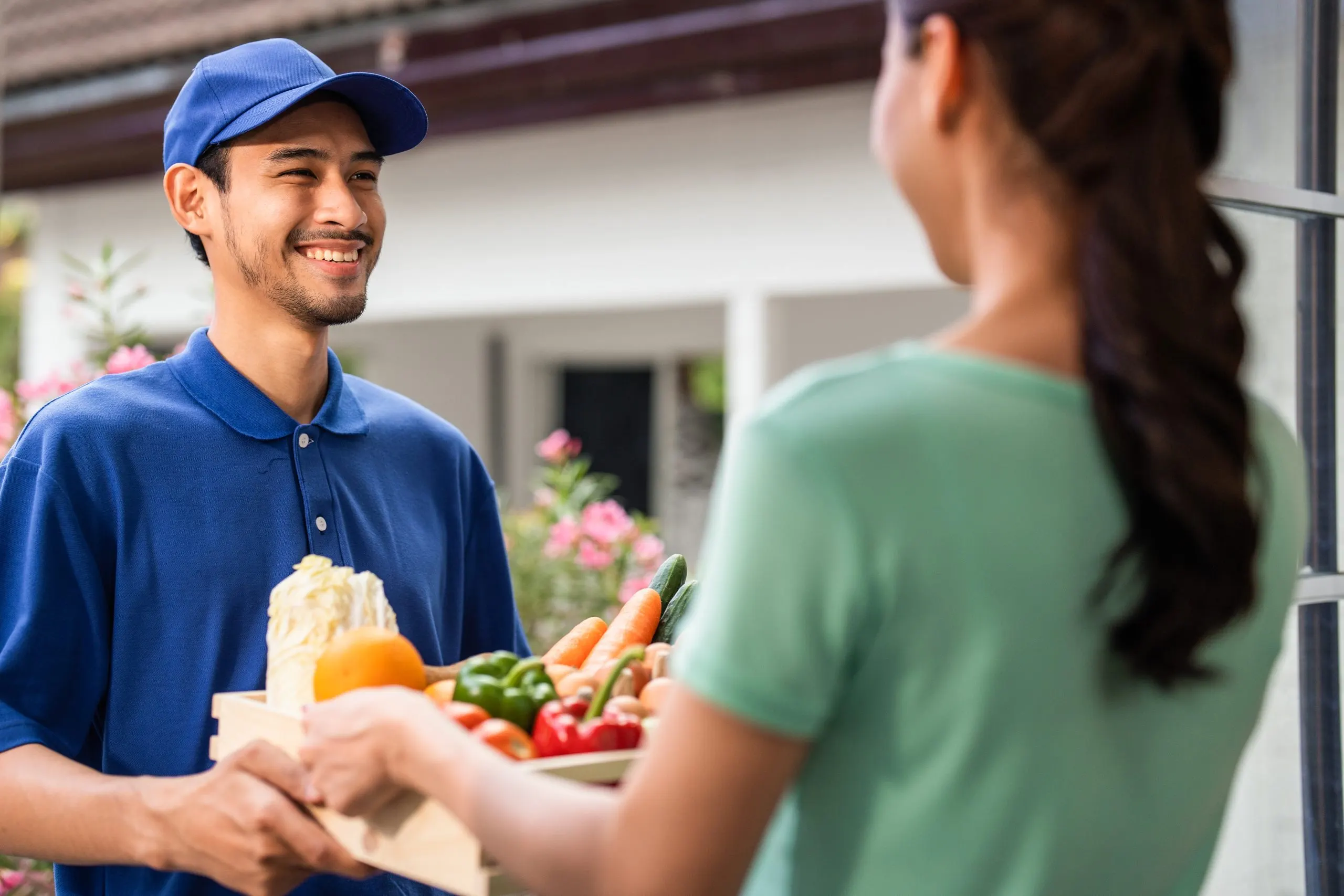 USA CEP Market Outlook to 2035 asian-young-delivery-man-delivering-package-female-customer-home-attractive-postman-blue-uniform-working-deliver-box-fruit-vegetable-groceries-woman-infront-door-house-scaled