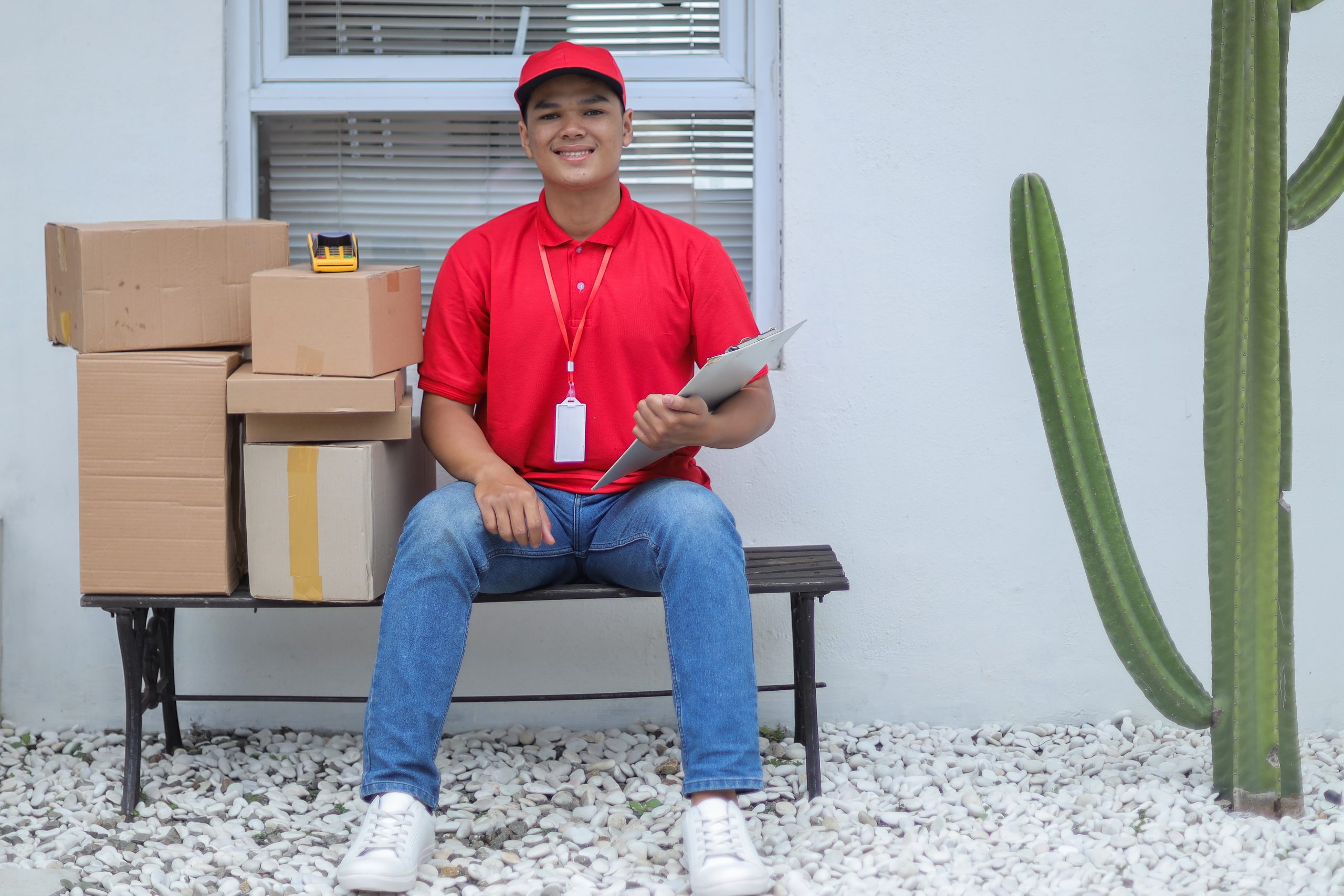 portrait-young-deliveryman-sitting-bench-with-stack-packages-scaled