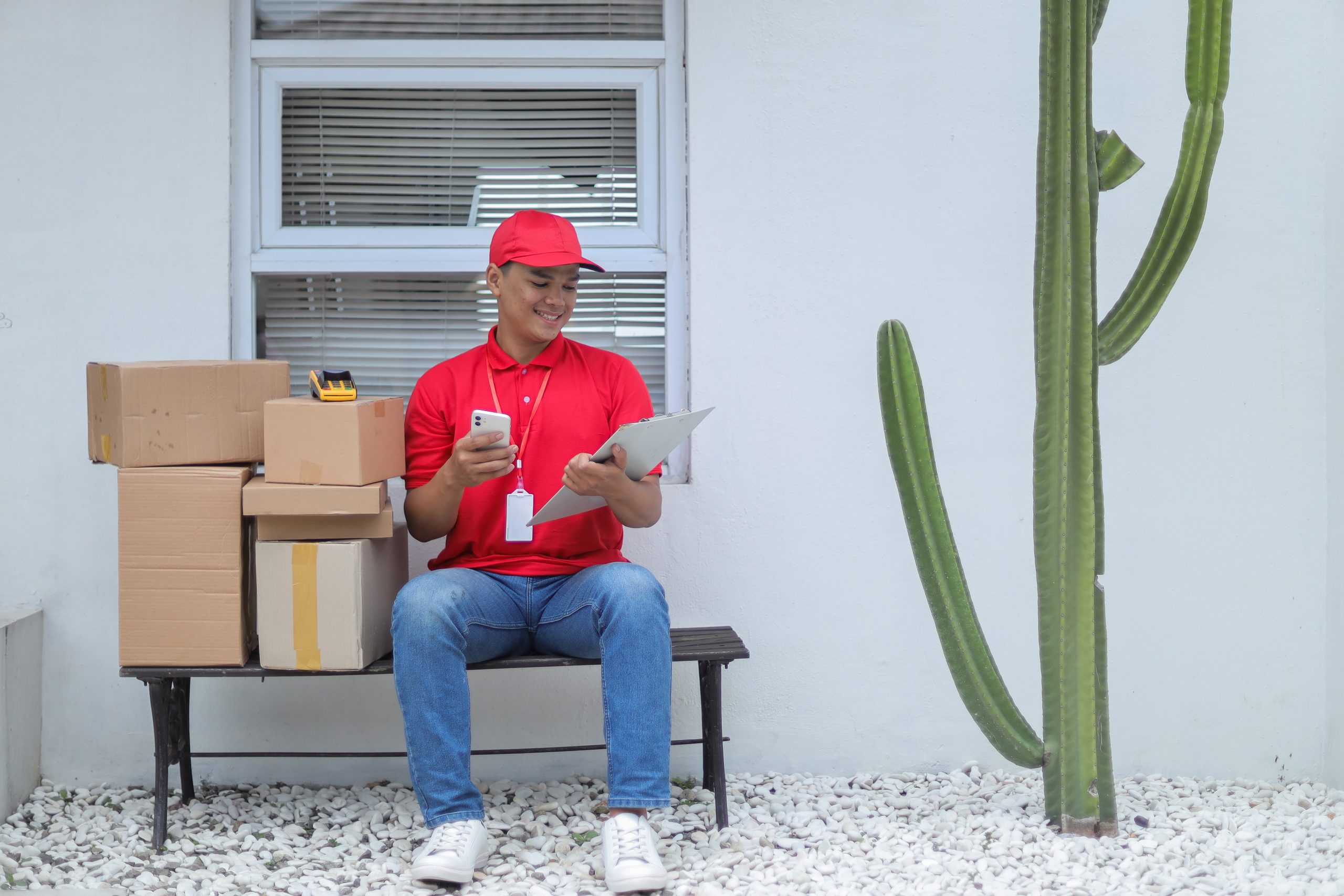 young-deliveryman-sitting-bench-with-stack-packages-checking-documents-outdoor-scaled