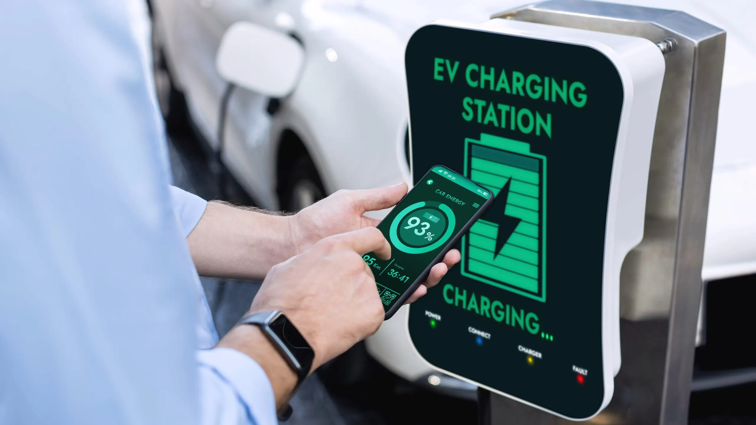A Look into Malaysia’s Growing EV Battery Management System Market with EV Registrations Hitting ~44,800 Units in the coming years businessman-holding-smartphone-display-battery-status-interface-by-smart-ev-mobile-application-while-ev-car-recharging-electricity-from-charging-station-car-park-peruse-1-scaled