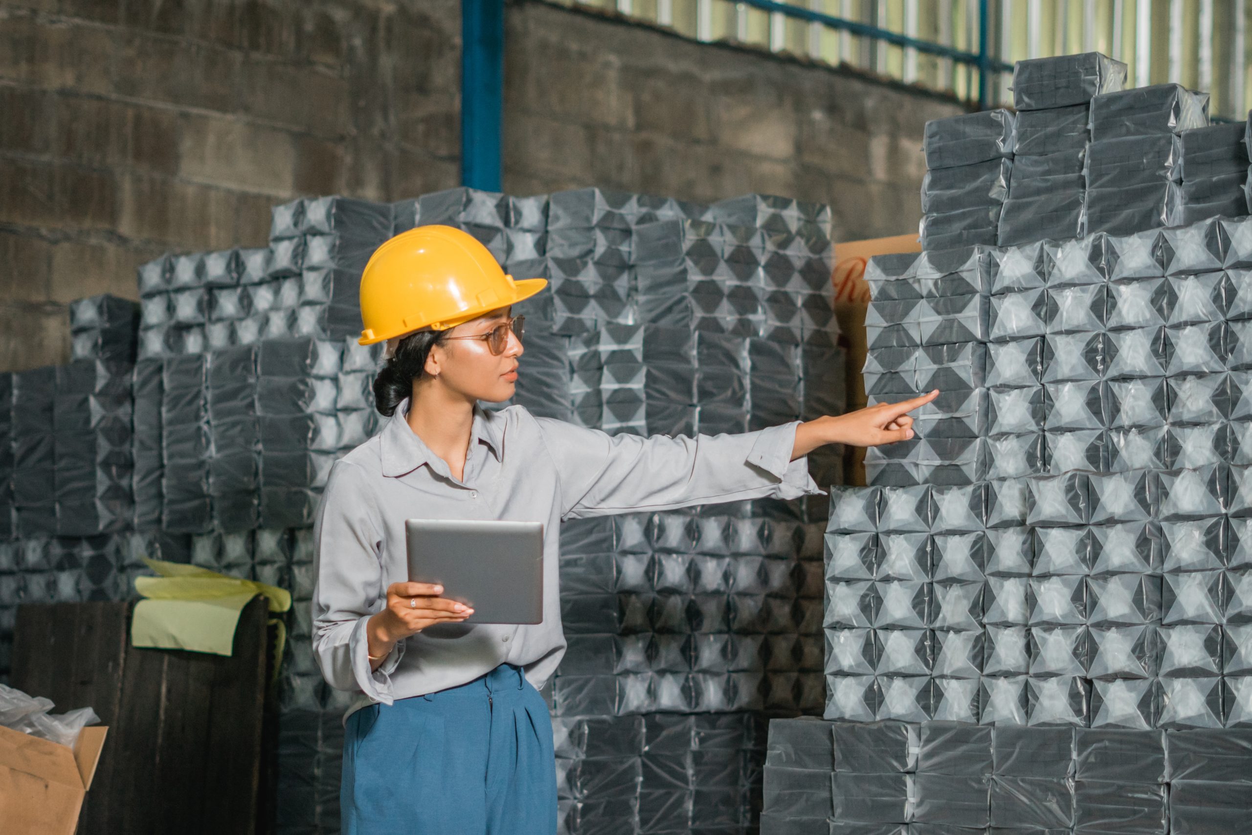 female-company-employee-standing-with-finger-pointing-holding-tab-while-working-storage-scaled