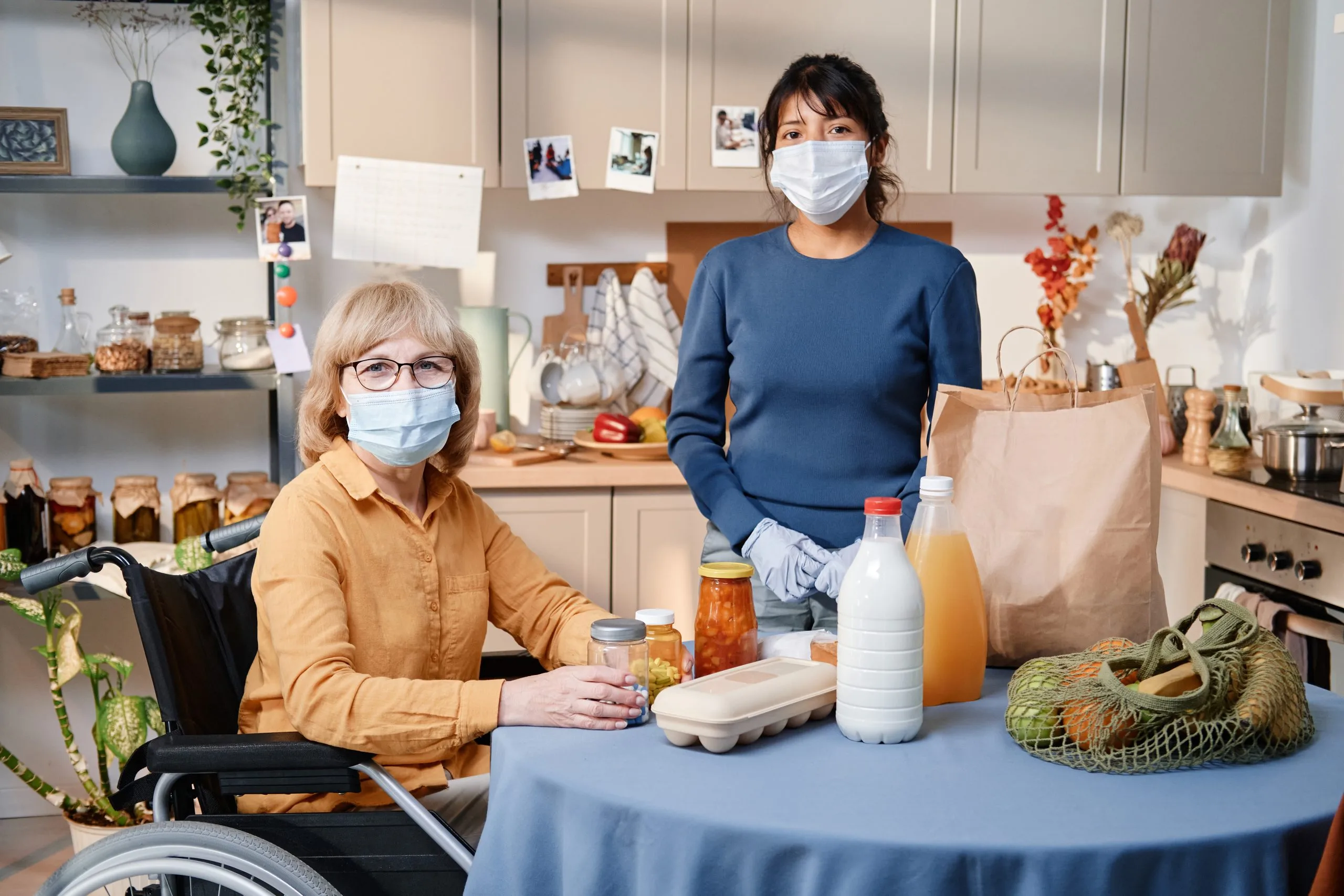 UK Home Care Market Outlook to 2035 portrait-senior-woman-using-wheelchair-sitting-table-with-products-looking-camera-with-caregiver-standing-near-by-they-wearing-masks-scaled