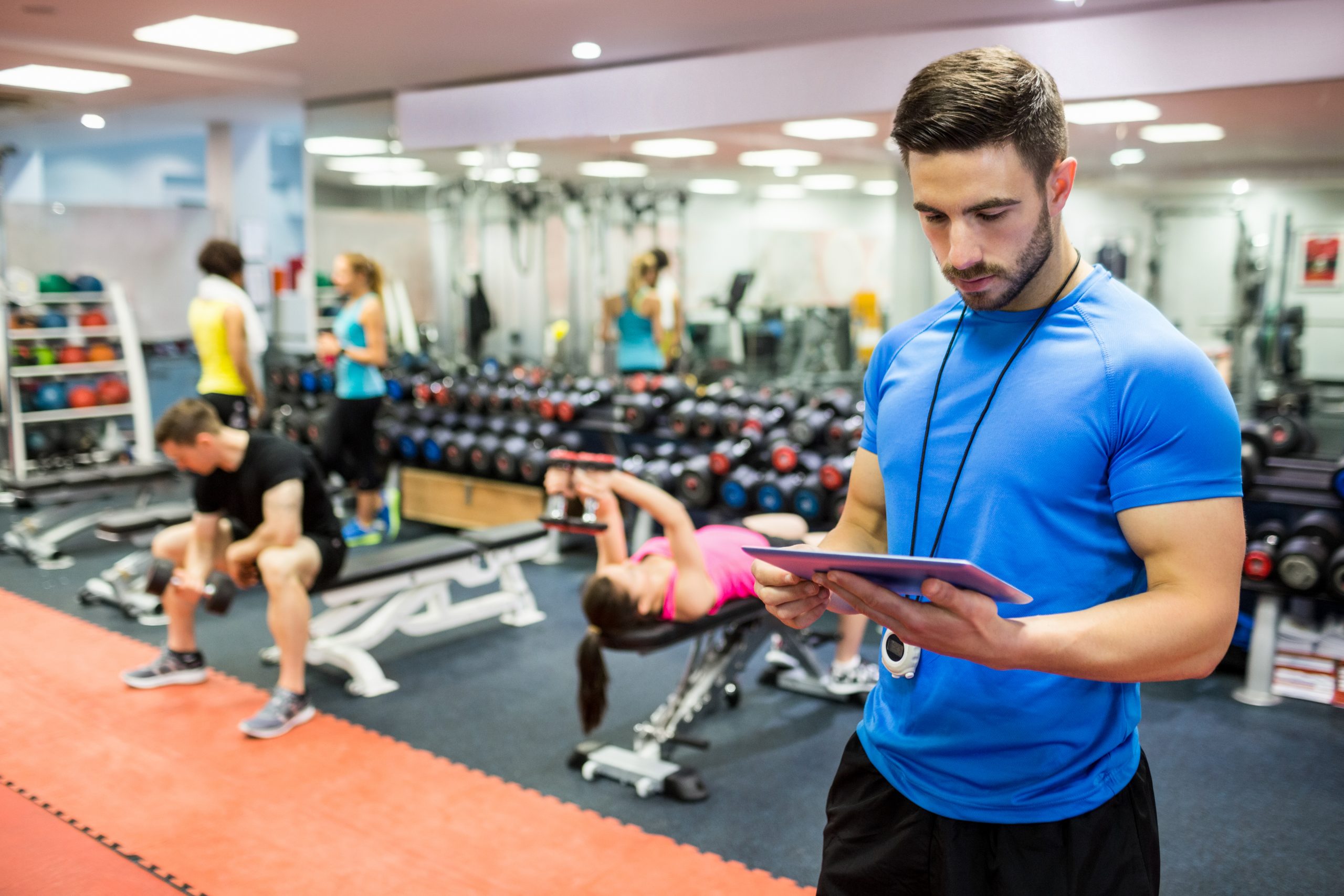 handsome-trainer-using-tablet-weights-room-scaled