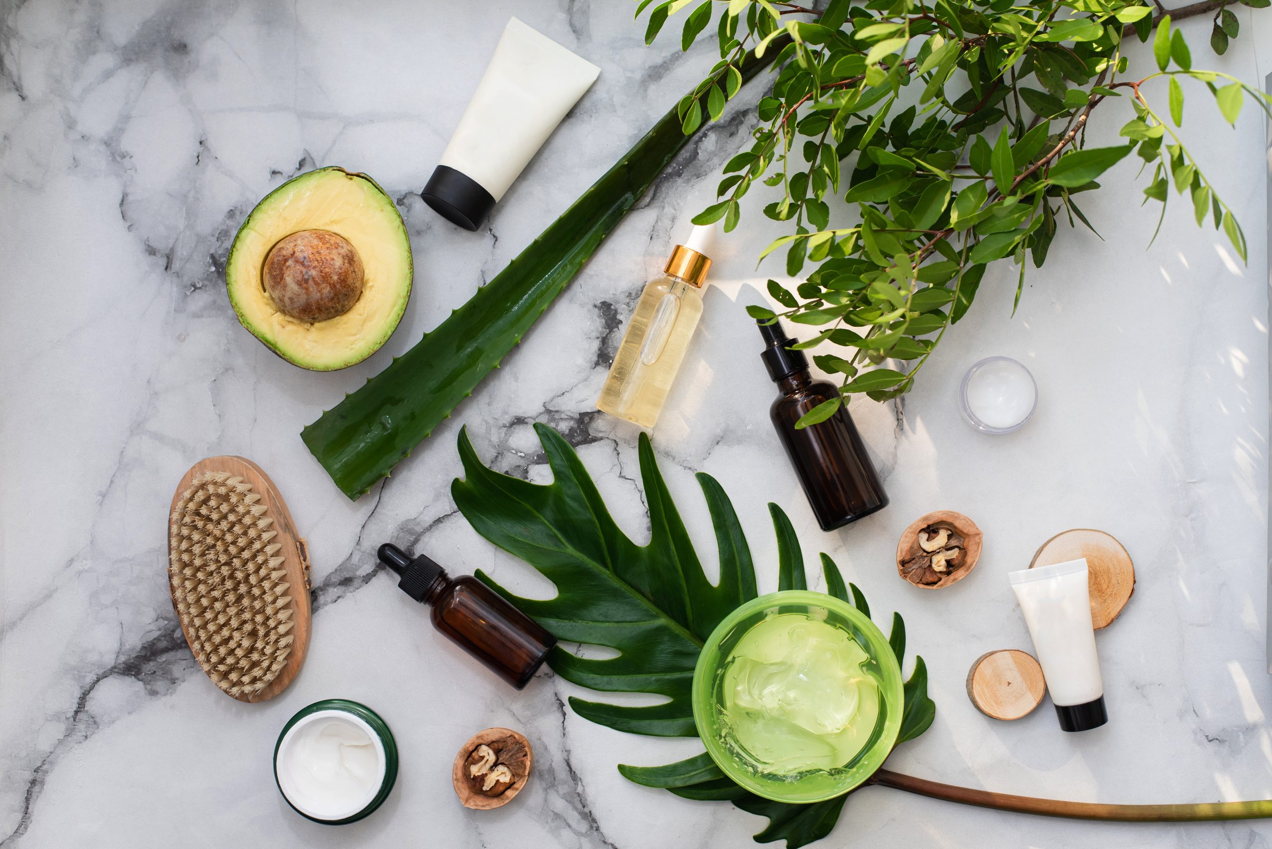 natural-cosmetics-with-herbal-ingredients-flat-lay-bottles-essential-oils-jar-moisturizer-green-leaves-white-stone-marble-background-scaled