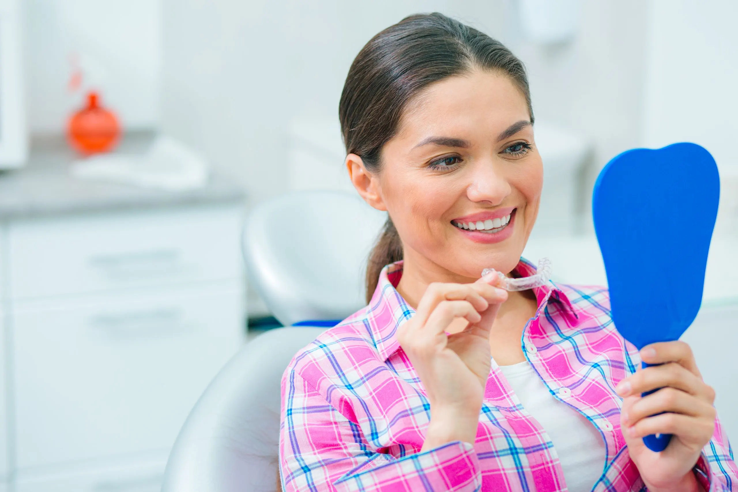 Singapore Teeth Whitening Market Outlook to 2035 positive-woman-sitting-dental-chair-with-dental-plate-hand-looking-her-reflection-mirror-scaled