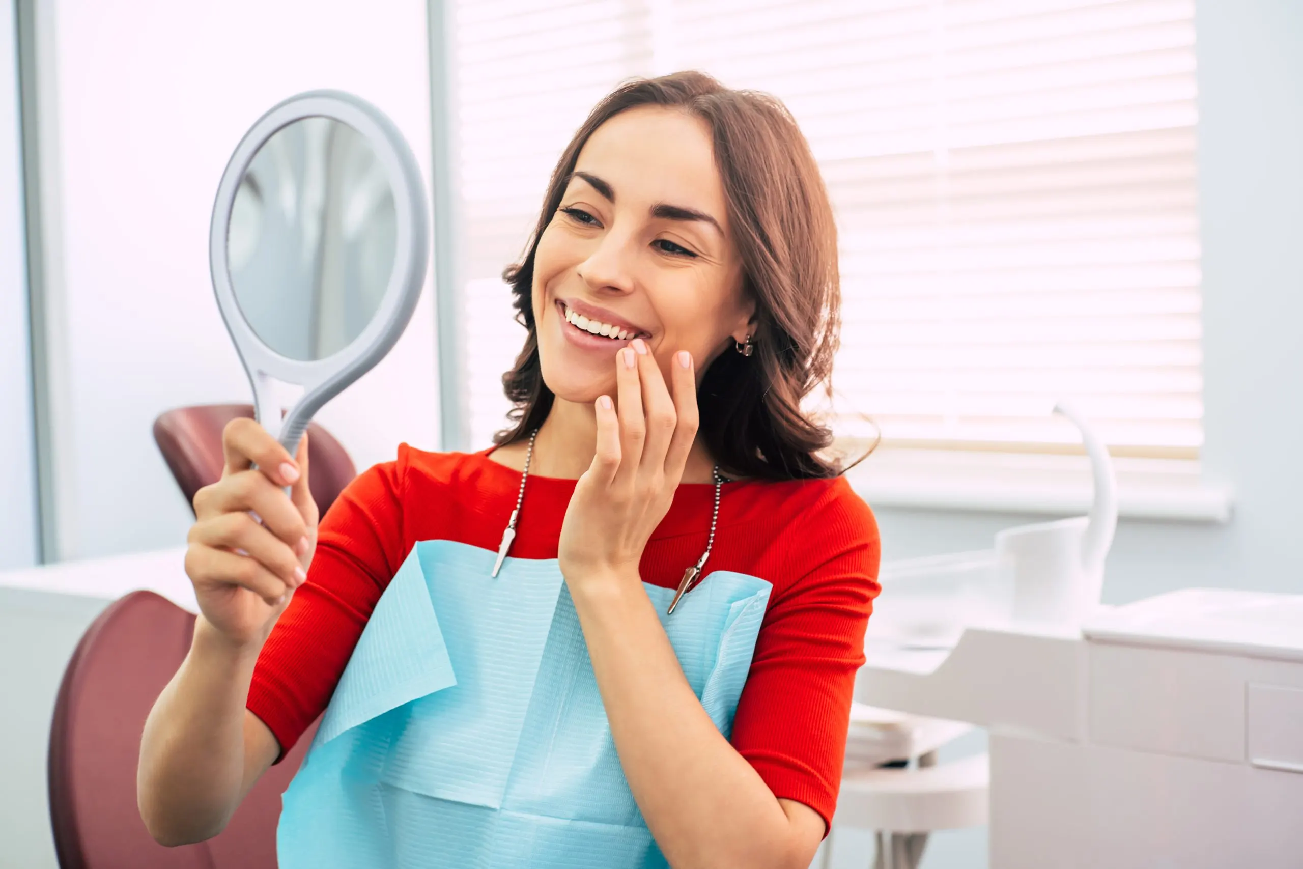 Brazil Teeth Whitening Market Outlook to 2035 pretty-girl-dentist-cabinet-is-using-mirror-look-through-ideal-work-doctor-she-has-special-dentist-napkin-her-vibrant-red-sweater-scaled