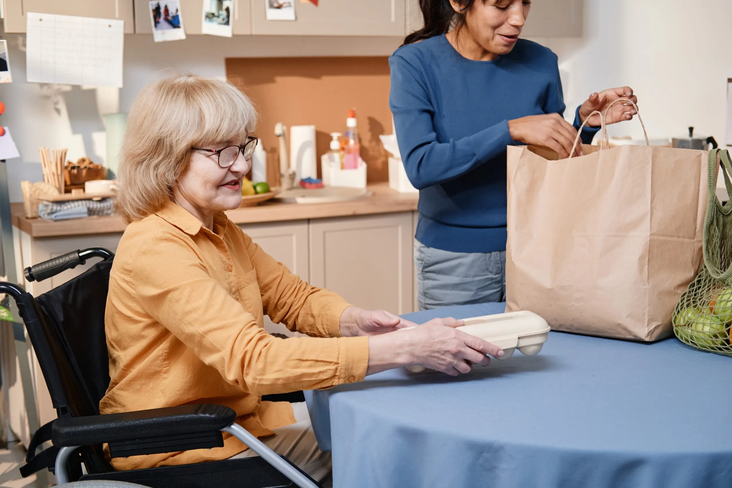 USA Home Care Market Outlook to 2035 senior-woman-sitting-wheelchair-table-she-getting-food-from-volunteer-who-delivering-it-home-scaled