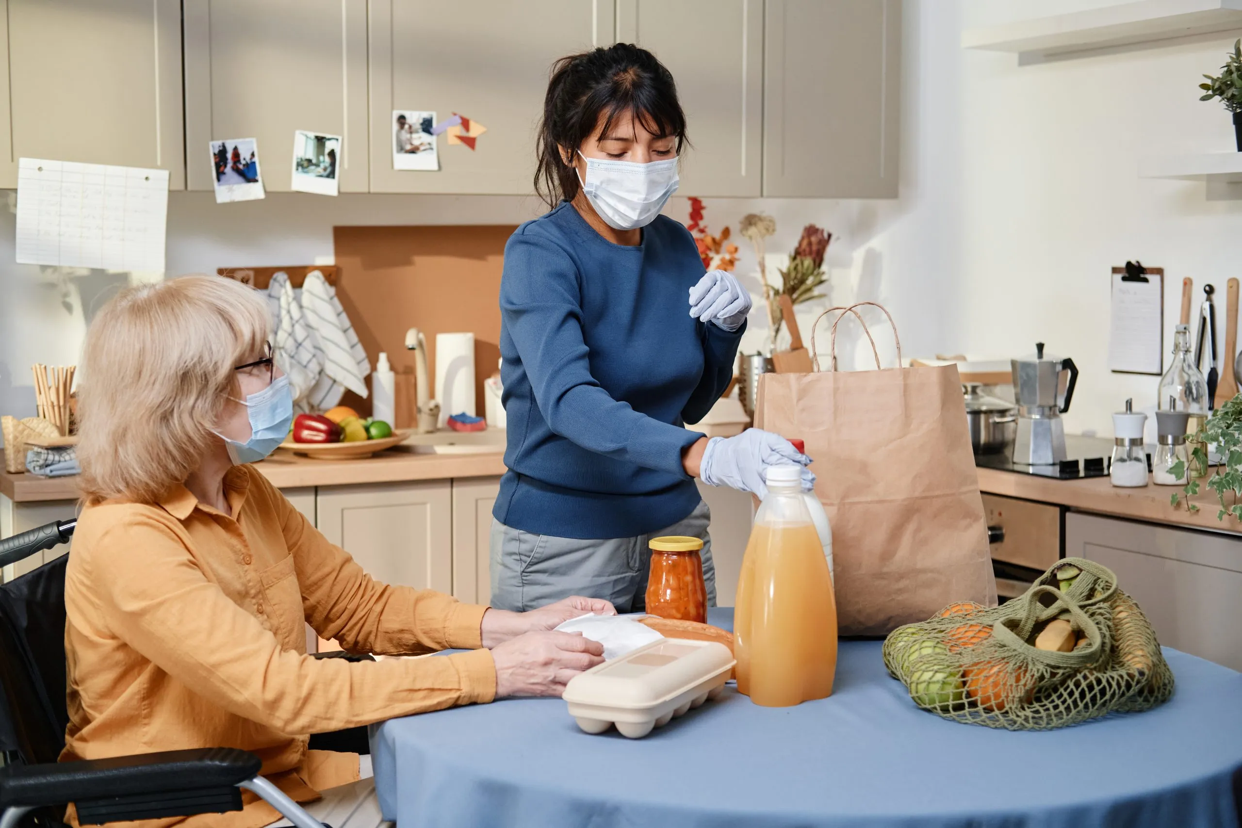 KSA Home Care Market Outlook to 2035 volunteer-mask-delivering-food-senior-woman-who-using-wheelchair-they-sitting-table-kitchen-scaled