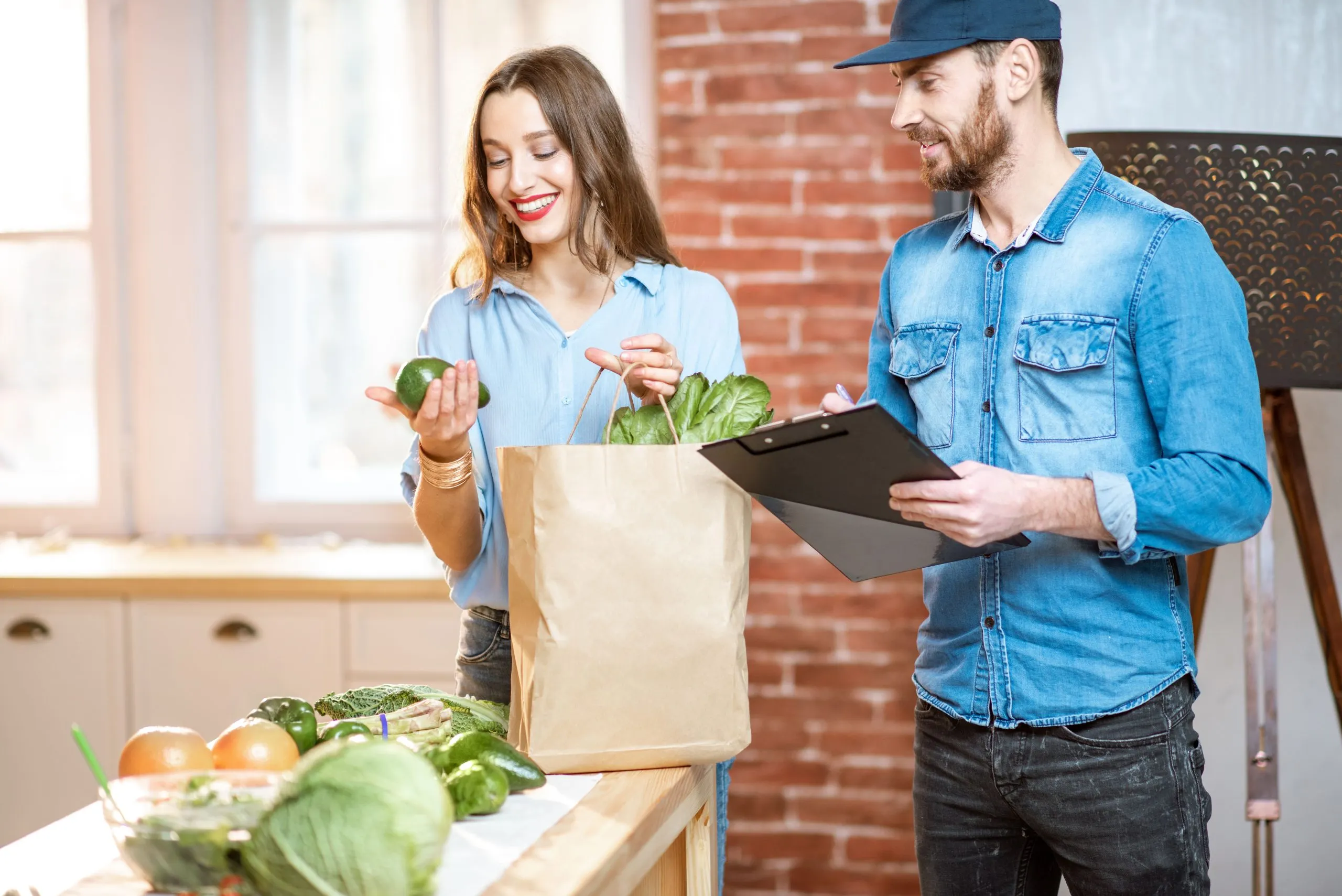 South Africa Online Grocery Delivery Market Outlook to 2035 woman-client-cheking-products-standing-with-delivery-worker-kitchen-home-1-scaled
