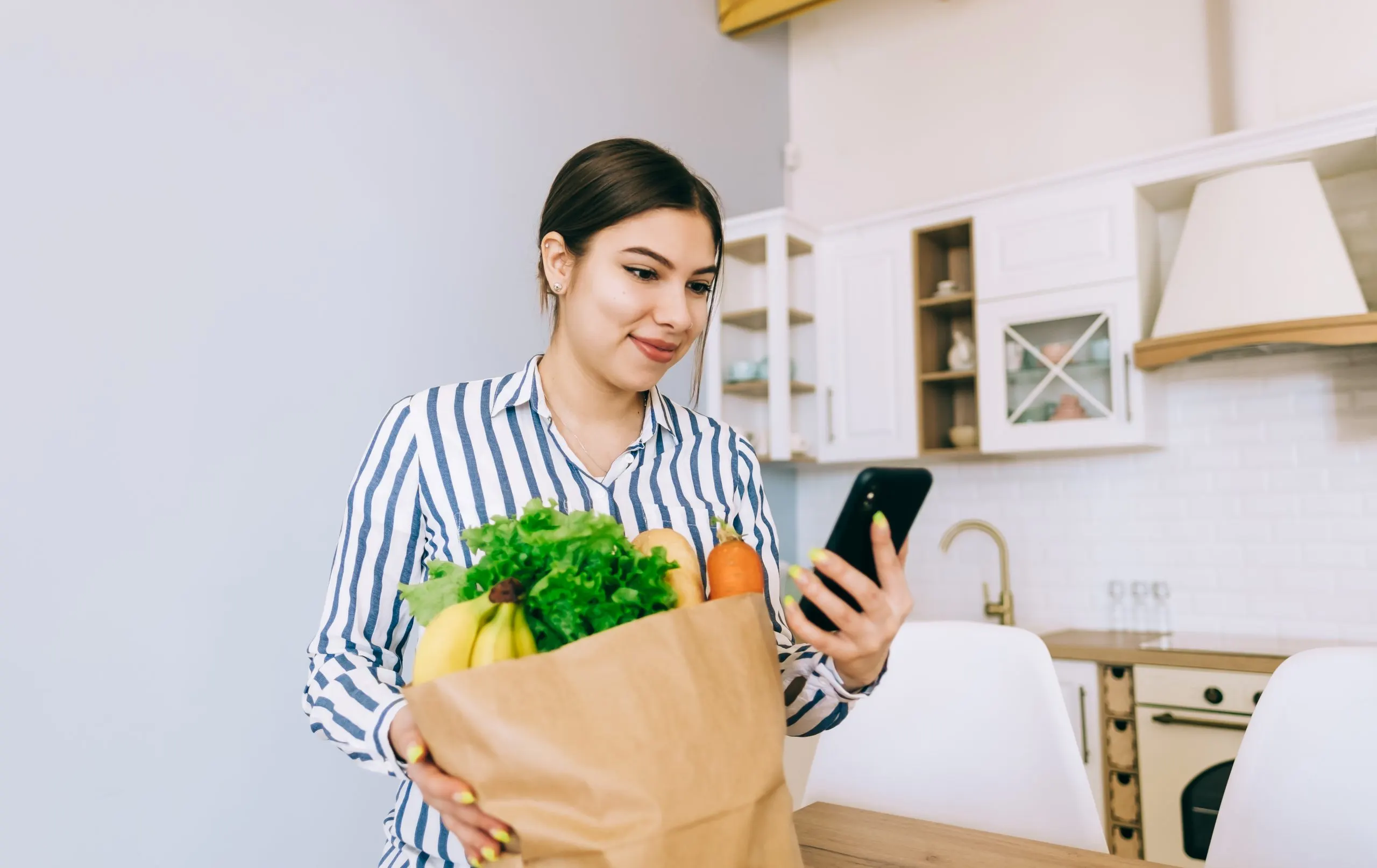 India Online Grocery Delivery Market Outlook to 2035 young-smiling-caucasian-woman-use-smartphone-modern-kitchen-bag-with-fresh-vegetable-table-online-buying-food-grocery-scaled