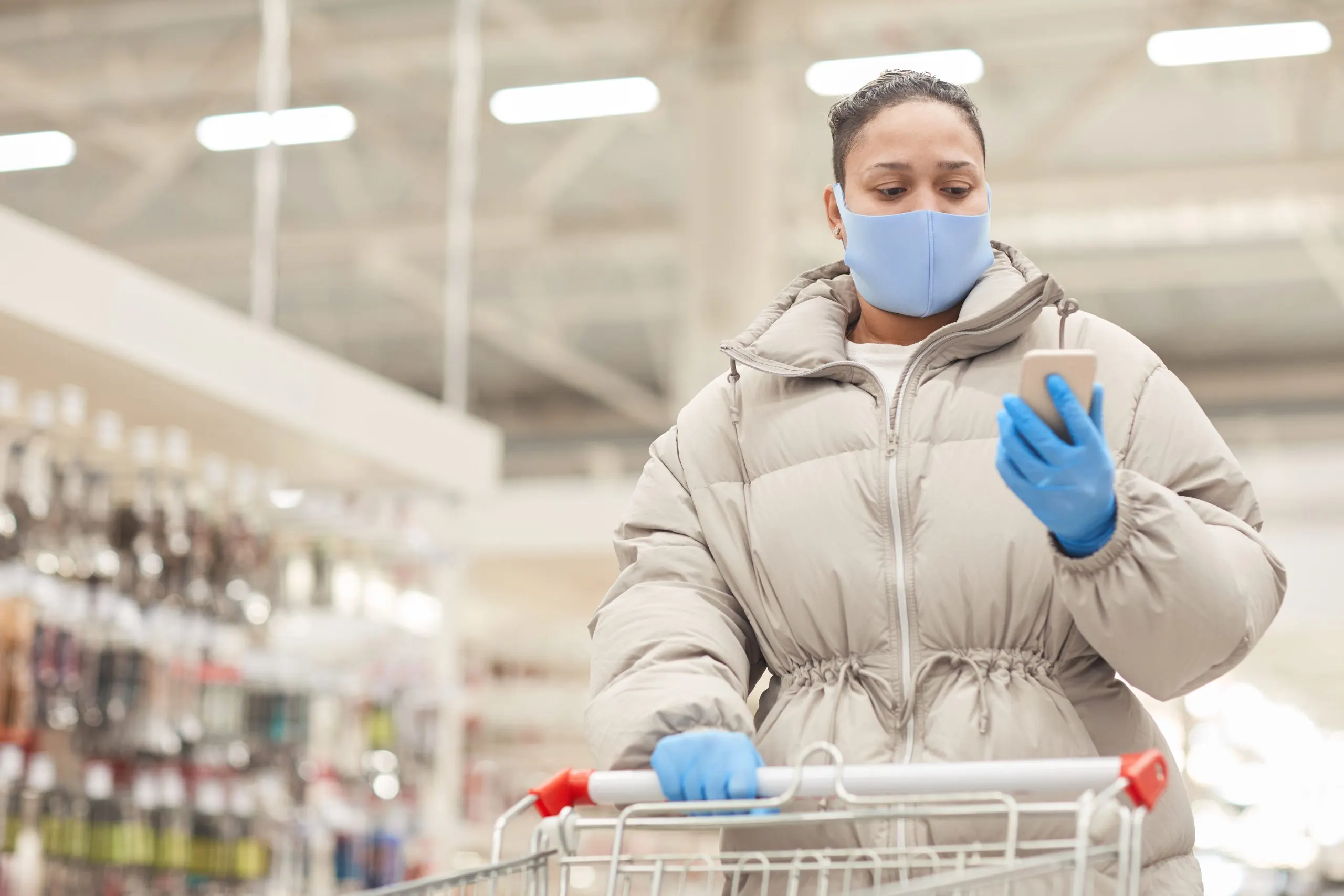 KSA Hand Gloves Market Outlook Highlighting $180M Revenue and 8% CAGR Key Drivers and Trends young-woman-protective-gloves-mask-reading-message-her-mobile-phone-while-doing-shopping-with-cart-supermarket-scaled