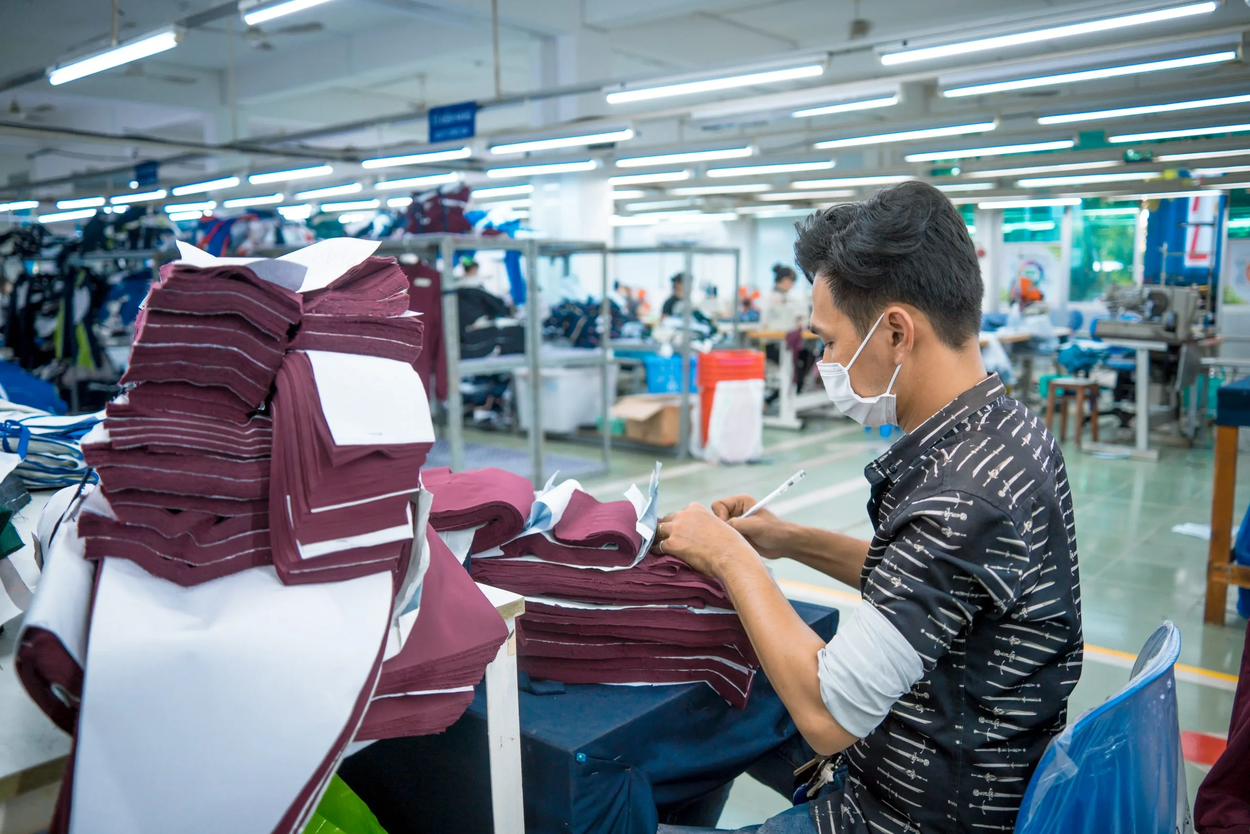 Brazil Duty Free And Travel Retail Market Outlook to 2035 two-asian-man-wearing-medical-mask-writing-number-fabric-after-finished-cut-textile-cloth-factory-working-process-tailoring-workers-equipment-scaled